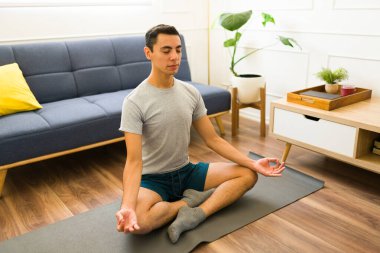 Gri bir tişört giyen rahat genç adam yoga ya da nefes egzersizleri sırasında meditasyon yapıyor. 