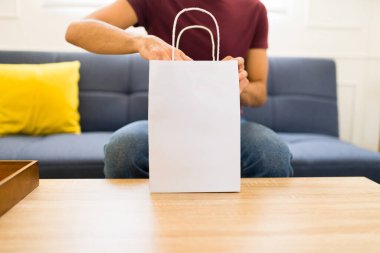 Oturma odasında, içinde fotokopi alanı olan boş bir alışveriş çantası olan genç bir latin adam var. 