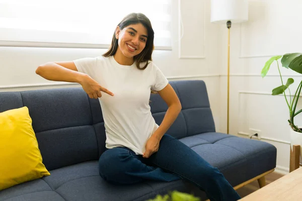 自宅でリラックスしながら白いモックアップTシャツの彼女のロゴデザインを指す美しい幸せな女性 — ストック写真
