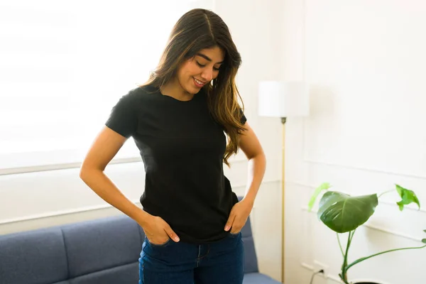 西班牙裔年轻女性在家里展示着她那件黑色仿T恤的设计图案 看上去很开心 — 图库照片