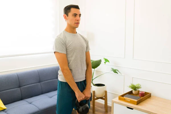一个活泼的年轻人穿着灰色的模拟T恤在家里提起水壶的重量 — 图库照片
