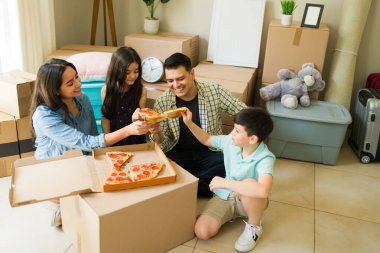 Bir sürü kutuyla taşındıktan sonra anneleri ve babalarıyla birlikte yeni evlerinde pizza yiyorlar.