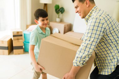 Mutlu baba ve oğlu, karton kutuları açarken gülümsüyor ve yeni bir eve ya da daireye taşınıyorlar.