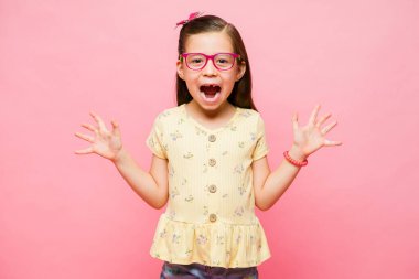 Heyecanlı beyaz ilkokul kızı çığlık atıyor pembe arka planda korkmuş görünerek göz teması kuruyor.