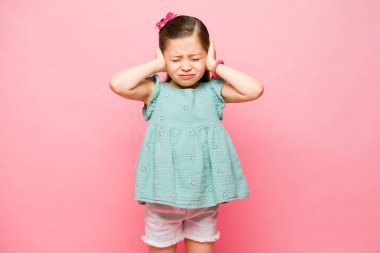 Kulaklarını pembe bir stüdyonun arka planına tıkayan gürültüden rahatsız olan ilkokul çocuğu.