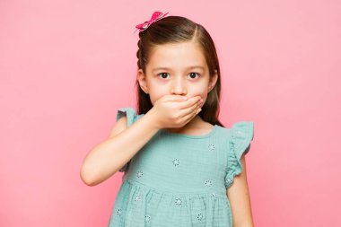 Korkak küçük kız 7 yaşında. Pembe arka planda bağırmayı kesmesi için ağzını kapatmış gibi görünüyor.