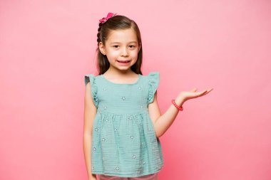 Kafkasyalı mutlu küçük çocuk elinde sahte bir ürünle gülümsüyor ve pembe bir arka planda mutlu görünüyor.