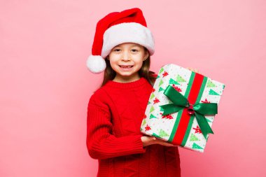 Heyecanlı bir ilkokul çağının portresi. Küçük bir kız Noel hediyeleri alıyor ve Noel Baba şapkasıyla bayramları kutluyor.