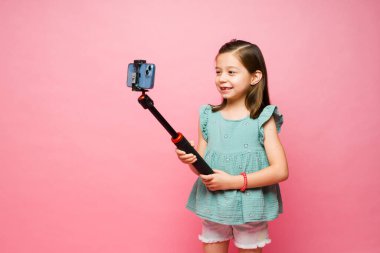 Akıllı bir telefonla selfie çubuğuyla video çekerken ya da fotoğraf çekerken gülümseyen sevimli küçük kız. 