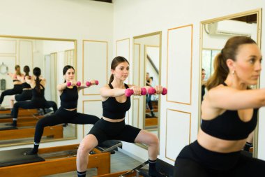 Güzel bir genç kadın pilates kursunda yüksek kalitede bir spor salonunda halterlerle egzersiz yapıyor.