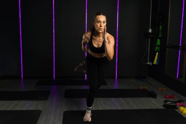 Aktif formda genç bir kadın kardiyo HIIT egzersizi yapıyor ya da yüksek kalitede karanlık bir spor salonunda ışıkla çapraz antrenman yapıyor.