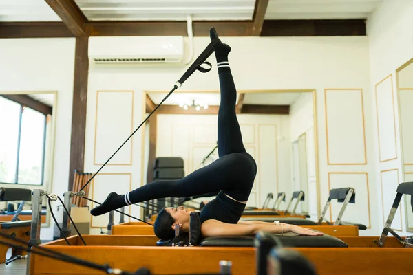 在健身房上普拉提课时 灵活的高加索女人在床改革者中锻炼她的核心和伸展她的腿 — 图库照片
