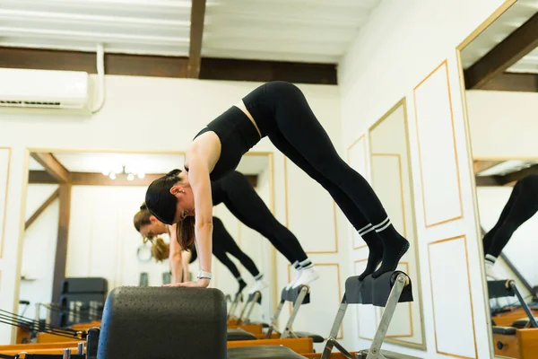 在健身中心的普拉提课上 女运动员使用床改头换面和做木板运动的侧视图 — 图库照片