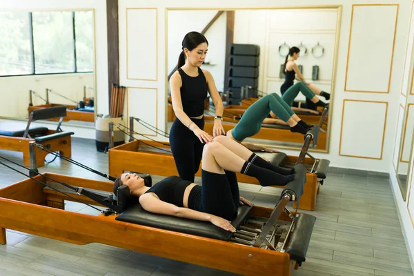 Pilates coach at a beautiful high-end gym giving a class to young women using reformer beds during a fit workout