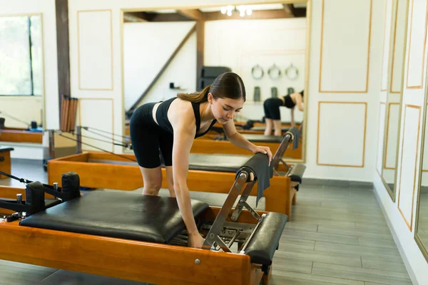 Sporty young woman at a high-end fitness center working out on a bed reformer training during a pilates class