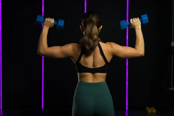 一名体格健壮的年轻女子在体育馆提起哑铃举重时 从后面露出她强壮的肌肉后背 — 图库照片