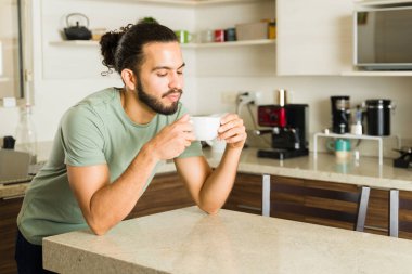 Yakışıklı İspanyol bir adam bir fincan kahve içip ev işlerinden önce mutlu görünerek ev hayatından zevk alıyor.