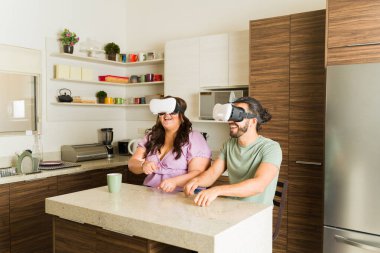 Mutfaktaki neşeli Latin çift evde sanal gerçeklik VR gözlükleri teknolojisi kullanarak rahatlıyor ve birlikte eğleniyorlar.