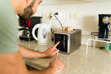 Sabah mutfakta kahvaltı hazırlarken tost makinesine ekmek koyarken gülümseyen genç bir adamın yakın plan fotoğrafını çek.