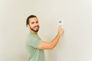 Klimayı açarken gülümseyen ve evdeki termostatı kullanan neşeli yakışıklı adam mutlu görünüyor.