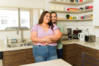 Romantik, çekici çift, mutfakta sarılırken gülümsüyor. Mutlu görünüyorlar. Ev ve ev işlerinin keyfini çıkarıyorlar.