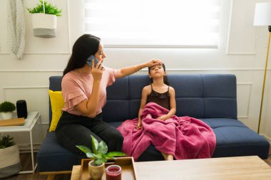 Meksikalı anne, hasta çocuğunun ateşini kontrol ediyor ve doktor muayenesi için bir çocuk doktorunu arıyor.