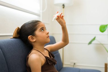 Sevimli İspanyol küçük kız hasta hissediyor. Kanepede tek başına otururken göz damlası ya da ilaç veriyor.