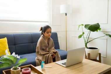 Küçük sevimli hasta kız battaniyeye sarılıp üşütmüş ya da ateşler içinde evde sanal bir doktorla konuşmuş.