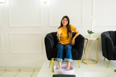 Mimoza kokteyli içerek gülümseyen güzel bir kadın manikürcüde dinleniyor ve rahatlatıcı bir pedikür hizmeti veriyor.