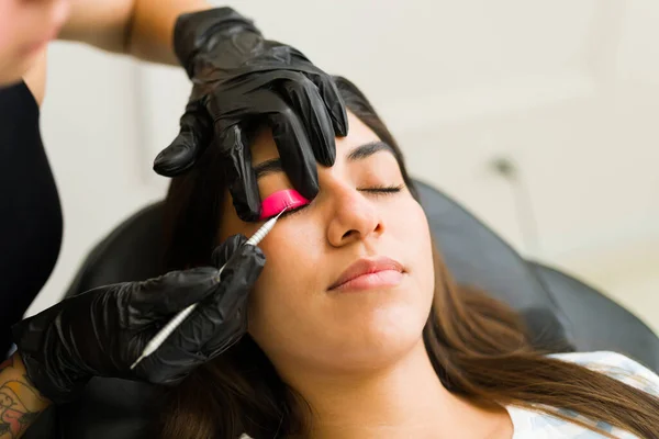 Attractive mexican young woman at the beauty salon doing lash extension service with the professional beautician