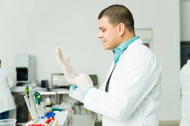 Beyaz laboratuvar önlüklü İspanyol profesyonel kimyager kan testleri yapan bir tıp laboratuarında eldiven giyiyor.