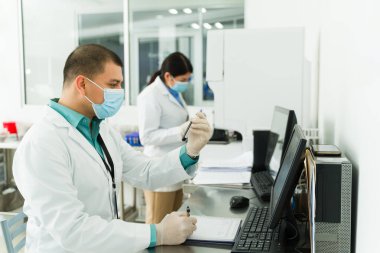Tıbbi laboratuvarda kan örnekleriyle çalışan Meksikalı kimyager test tüpleri kullanıyor ve bilgisayarda daktilo kullanıyor.
