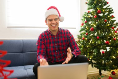 Noel Baba şapkalı heyecanlı İspanyol adam, Noel 'de partneriyle ya da ailesiyle konuşurken internetten yaptığı video konuşmasında gülüyor.