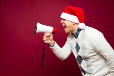 Heyecanlı bir Latin adamın profili megafonla bağırırken, Noel tatilini kırmızı arka planda fotokopi çekerek kutluyor.