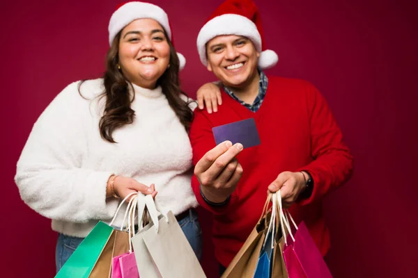 兴奋的拉丁裔夫妇笑着提着很多购物袋 用信用卡支付圣诞礼物 — 图库照片