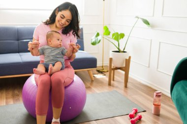 Mutlu ve aktif anne, yeni doğmuş bebeğiyle oynuyor. Evde antrenman yaptıktan sonra gülümsüyor.