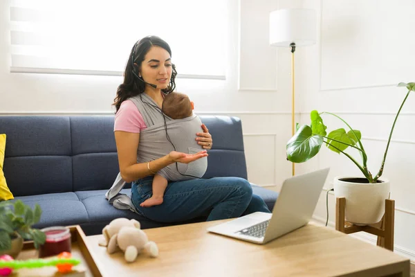 Working mother carrying her infant child using her newborn using a baby sling and working from home as a sales agent representative