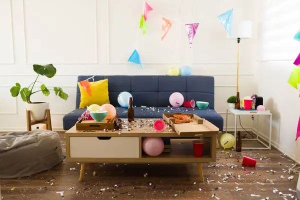 Living room home with confetti, balloons and party decorations having a disaster with trash and a mess after celebrating a birthday party
