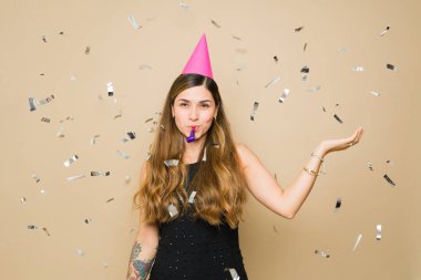 Çekici Latin bir kadın parti ıslığı çalıyor. Partide konfetiyle eğleniyor, gülümsüyor ve kutluyor.