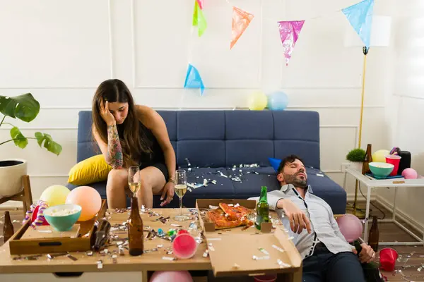 頭痛と吐き気のある病気の若い女性は 誕生日パーティー中に飲酒を祝った後 無意識の男性とハンガーを見ています — ストック写真