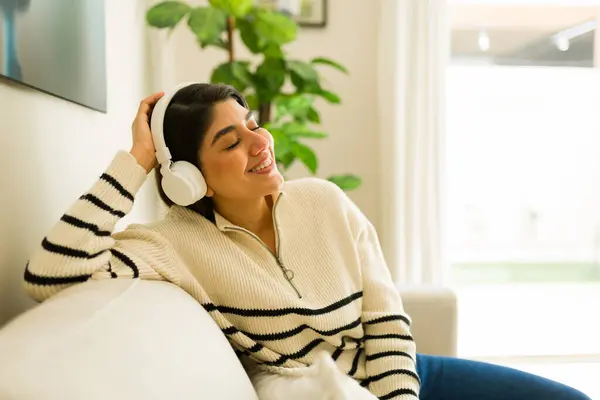 Happy relaxed woman in her 20s listening to music with headphones and relaxing on the sofa while enjoying leisure time at home