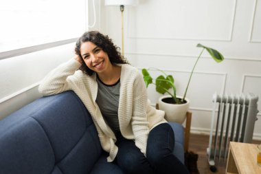 Evdeki kanepede dinlenirken gülümseyen ve güz boyunca ısınmanın keyfini çıkaran güzel Latin bir genç kadın.