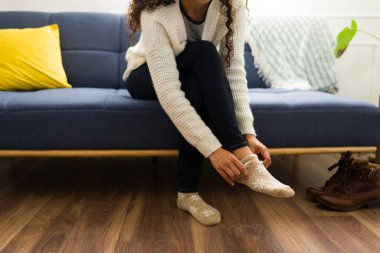 Evdeki soğuk havada ısınan genç bir kadının oturma odasındaki kanepede çorap ve kışlık giysilerini giymesi.