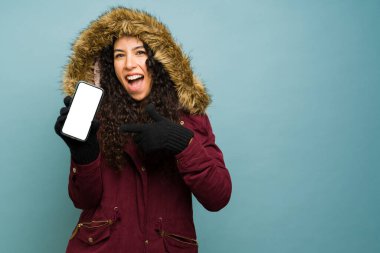 Soğuk havanın tadını çıkarırken sosyal medyayı kullanarak mesajlaşırken akıllı telefon ekranını gösteren heyecanlı Latin bir kadın.