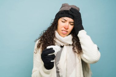 Kötü bir soğuk algınlığı ve kötü bir soğuk algınlığıyla baş ağrısı çeken ve kış havasında burnunu mendille silen genç bir kadın.