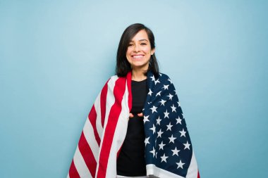 Güzel vatansever kadın Amerikan bayrağını kullanarak mutlu ve gülümseyen mavi bir arka plana karşı Amerikan rüyasının tadını çıkarıyor.