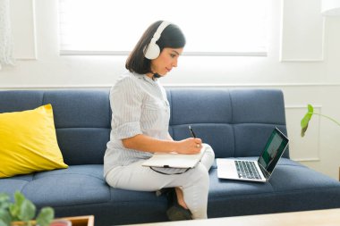 Kulaklıklı rahat kadın öğrenci oturma odasındaki bilgisayarı kullanarak sanal bir ders alıyor ve İngilizce öğreniyor.