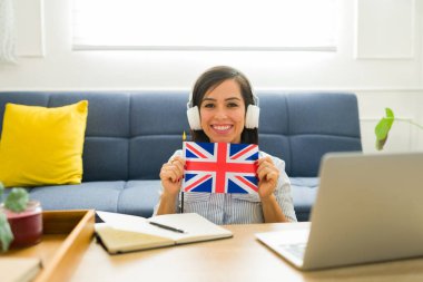İngiliz bayrağını elinde tutarak gülümseyen mutlu beyaz kadın İngilizce öğrenirken bir eğitim sitesi ya da uygulaması ile gururlanıyor