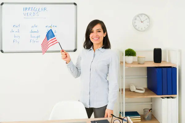 Smiling young woman and English teacher looking happy teaching English language while holding a US american flag