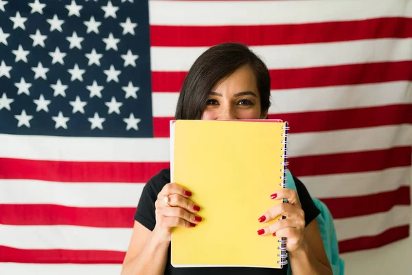 Surprised young woman hiding behind legal papers applying for a passport or green card visa smiling in front of the american US flag